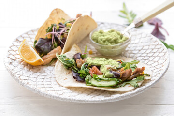 Plate with tacos and tasty guacamole in bowl on light wooden background, closeup