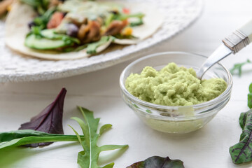 Tasty guacamole in bowl on light wooden background, closeup