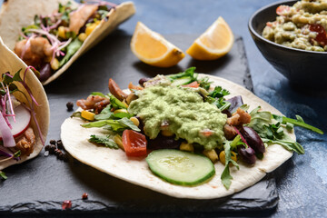Board with tacos and tasty guacamole in bowl on color background, closeup