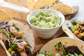 Board with tacos and tasty guacamole in bowl, closeup