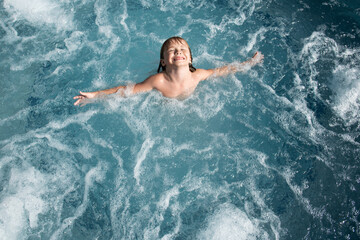 Young boy kid child splashing in swimming pool having fun leisure activity open arms.