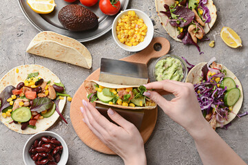 Woman making tasty tacos on grunge background