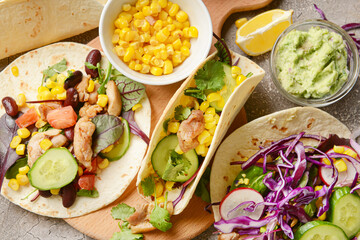 Board with tacos and tasty guacamole in bowl on grunge background