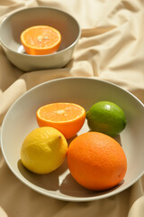 Bowls with healthy citrus fruits on light fabric background