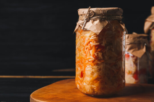 Glass jars with tasty sauerkraut on dark wooden background