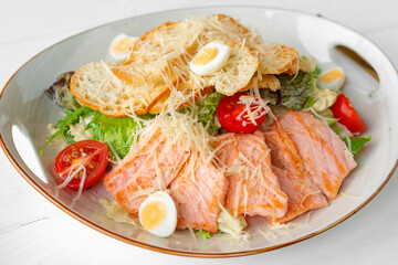 Caesar salad with grilled chicken on white wooden background