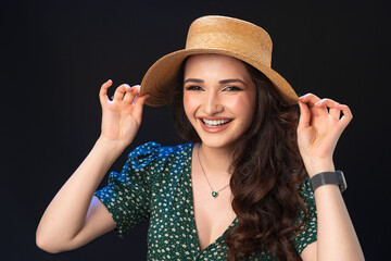 Beautiful young woman with straw hat posing against black background