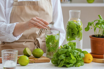 Woman making lemonade with basil on table in kitchen