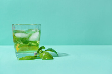 Glass of lemonade with basil on color background