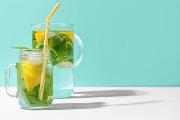 Mason jar and jug of lemonade with basil on color background