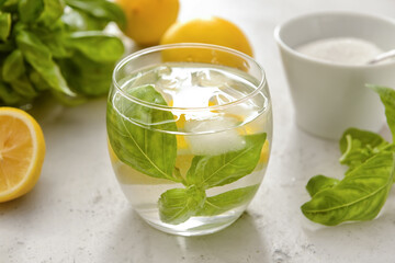 Glass of lemonade with basil on light background