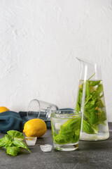 Glass and jug of lemonade with basil on light background