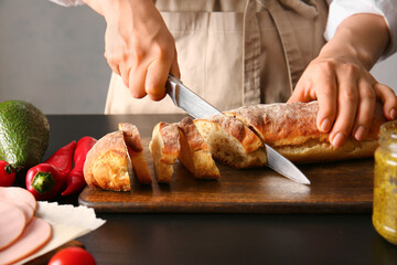 Woman cutting bread for tasty sandwiches on table