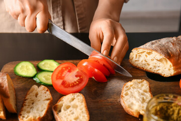 Woman cutting tomato for tasty sandwiches on table