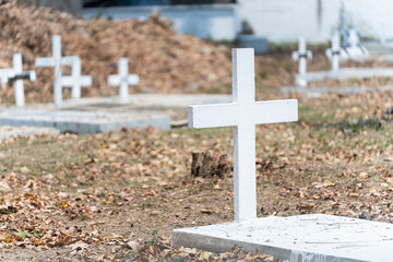A grave cross in a graveyard. Empty white stone cross against dry grass background in a Christian Cemetery.