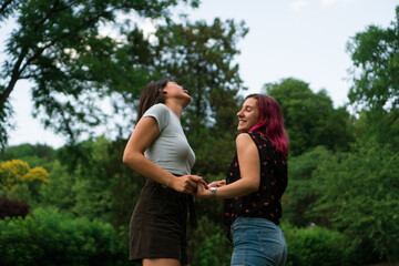 Two young women are dancing in the park and enjoying every moment. They are smiling from ear to ear.