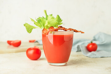 Glass of bloody mary cocktail garnished with bacon and tomatoes on light background