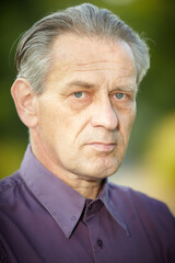 Older man in violet shirt posing in park for portrait