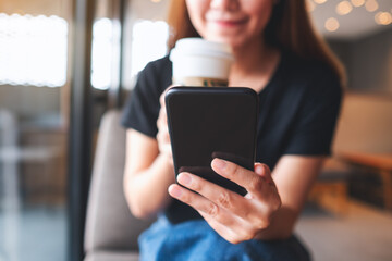 Closeup image of a beautiful young asian woman holding and using mobile phone while drinking coffee in cafe