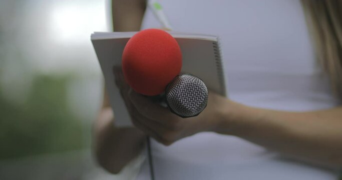 Female journalist at news event writing notes, holding microphone