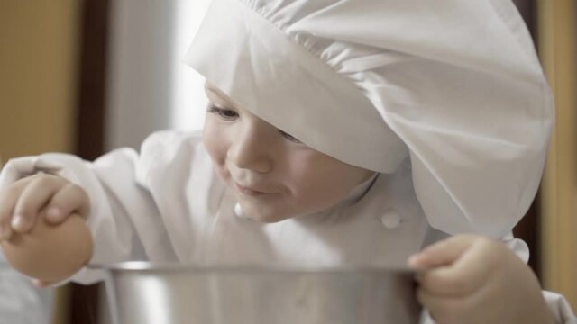 close-up of hands of a young chef learning to break eggs, hobby. ingredients to prepare cake. son with white chef uniform making a pie in his kitchen at home with his dad. Slow motion.