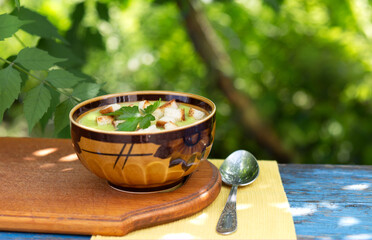 Creamy green pea soup with croutons and a sprig of parsley in a clay bowl on a rural table outside