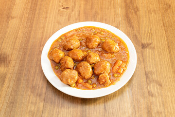 Main dish of meatloaf stewed with vegetables, baby carrots and peas in sauce on white plate and wooden table