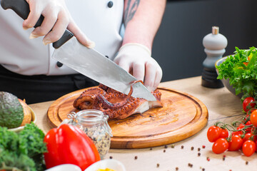 Young chef is cutting octopus in a modern kitchen. The man prepares food at home. Cooking healthy and tasty food.