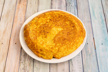 Spanish omelette cooked in a tapas restaurant with light wooden tables on white plate