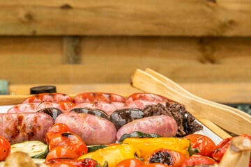 vegetables and sausages cooked on the grill with wooden tongs and wooden background a day of barbecue outdoors