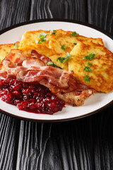 Swedish food potato pancakes with lingonberry jam and bacon close-up in a plate on the table. vertical