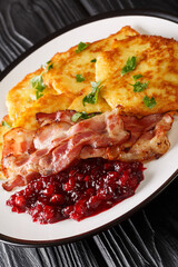 Raggmunk Crispy Swedish Potato Pancake with lingonberry jam and bacon close-up in a plate on the table. vertical