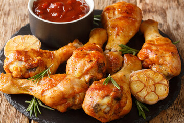 Hot fried chicken legs with garlic and rosemary served with bbq sauce close-up on a slate board on the table. horizontal