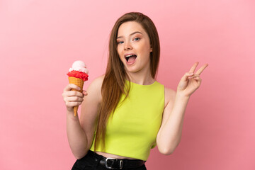 Teenager girl with a cornet ice cream over isolated pink background smiling and showing victory sign