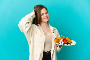 Teenager girl holding waffles over isolated blue background having doubts