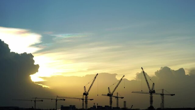 Cranes on the construction site or Big Container Cranes In The Port at sunset The sun gradually moved into the rain clouds, creating a beautiful rainbow light in the sky._construction background
