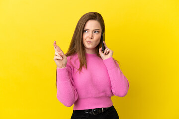 Teenager girl using mobile phone over isolated yellow background with fingers crossing and wishing the best