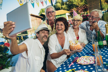 Senior people celebrating birthday in the cottage on the river having fun, make selfie photo.