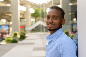 Portrait of handsome black African businessman outdoors in city during summer smiling