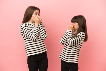 Little sisters girls isolated on pink background is a little bit nervous and scared putting hands to mouth