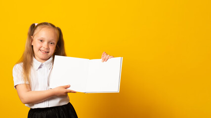 Education and school concept. Smiling little student girl with book. Copy space. Little kid looking at mockup poster and standing on yellow background.