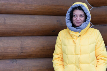 A woman in a bright yellow jacket stands against the backdrop of a log house and smiles. People, lifestyle concept