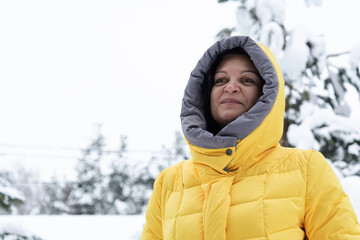 A woman in a bright yellow jacket smiles and walks in a snowy forest. People, lifestyle concept