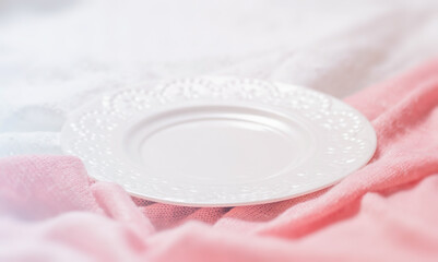 Fototapeta na wymiar Side view of a white plate against a background of pink and white cloth. 
