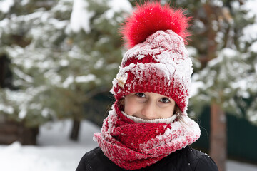 Teenage girl in a snow-covered red hat are standing against the background of trees and smiling. People, lifestyle concept