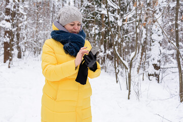 A woman in a bright yellow jacket holds a phone in her hands, smiles and walks in a snowy forest. People, lifestyle concept