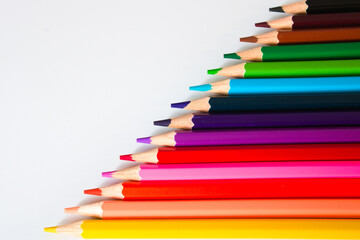 Coloured pencils in diagonal line, pointing to the left, isolated on white with copy space, top view