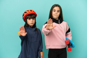 Little sisters practicing cycling and skater isolated on blue background making stop gesture denying a situation that thinks wrong