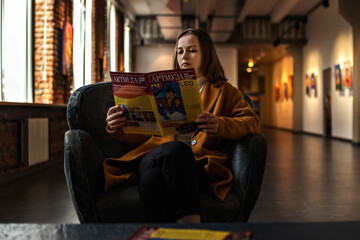 A young woman sits in a chair in the great hall of the art gallery looking through a booklet