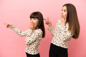 Little sisters girls isolated on pink background pointing finger to the side with a surprised face